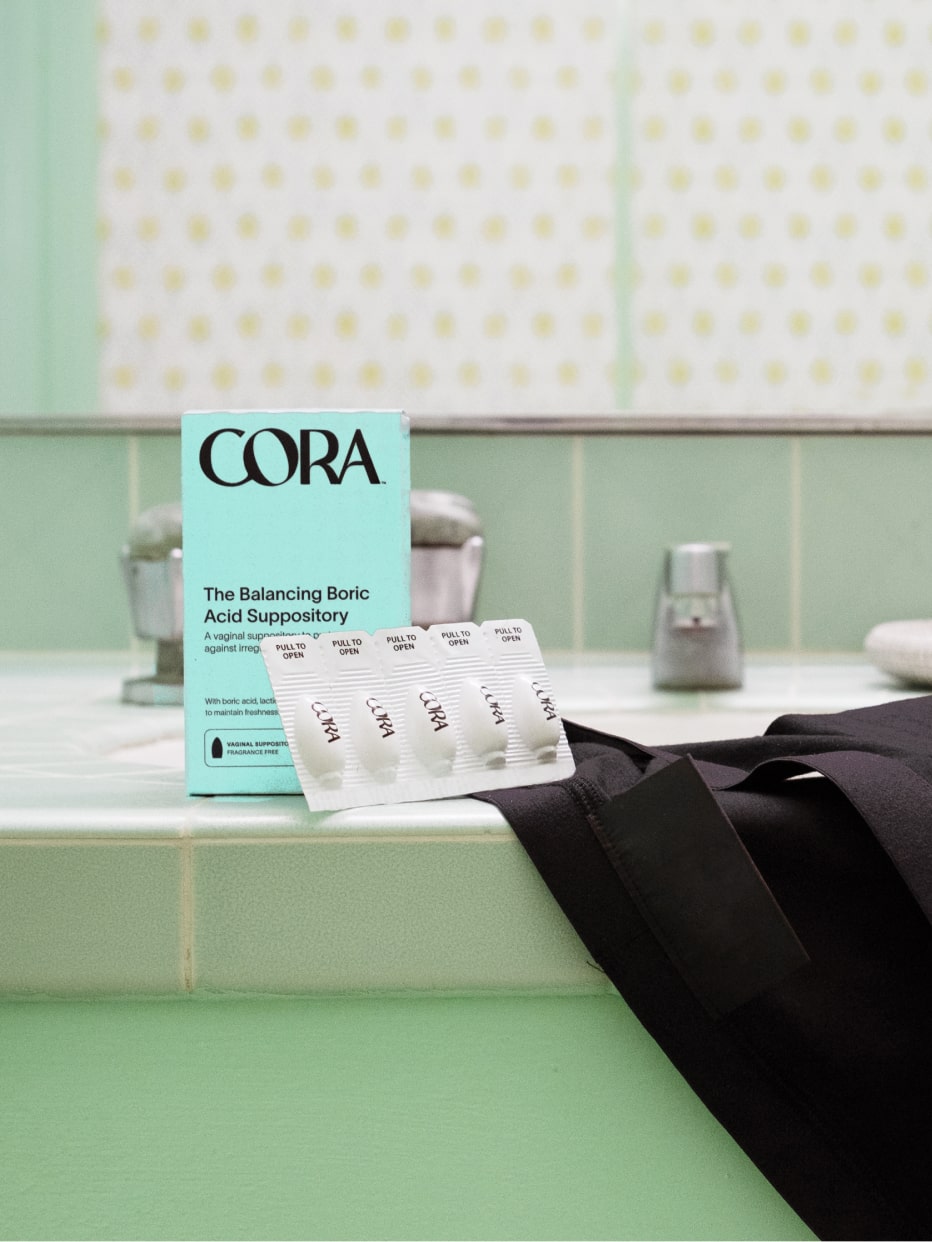 The Cora Boric Acid Suppository packaging and capsule product sitting upright on the edge of a bathtub