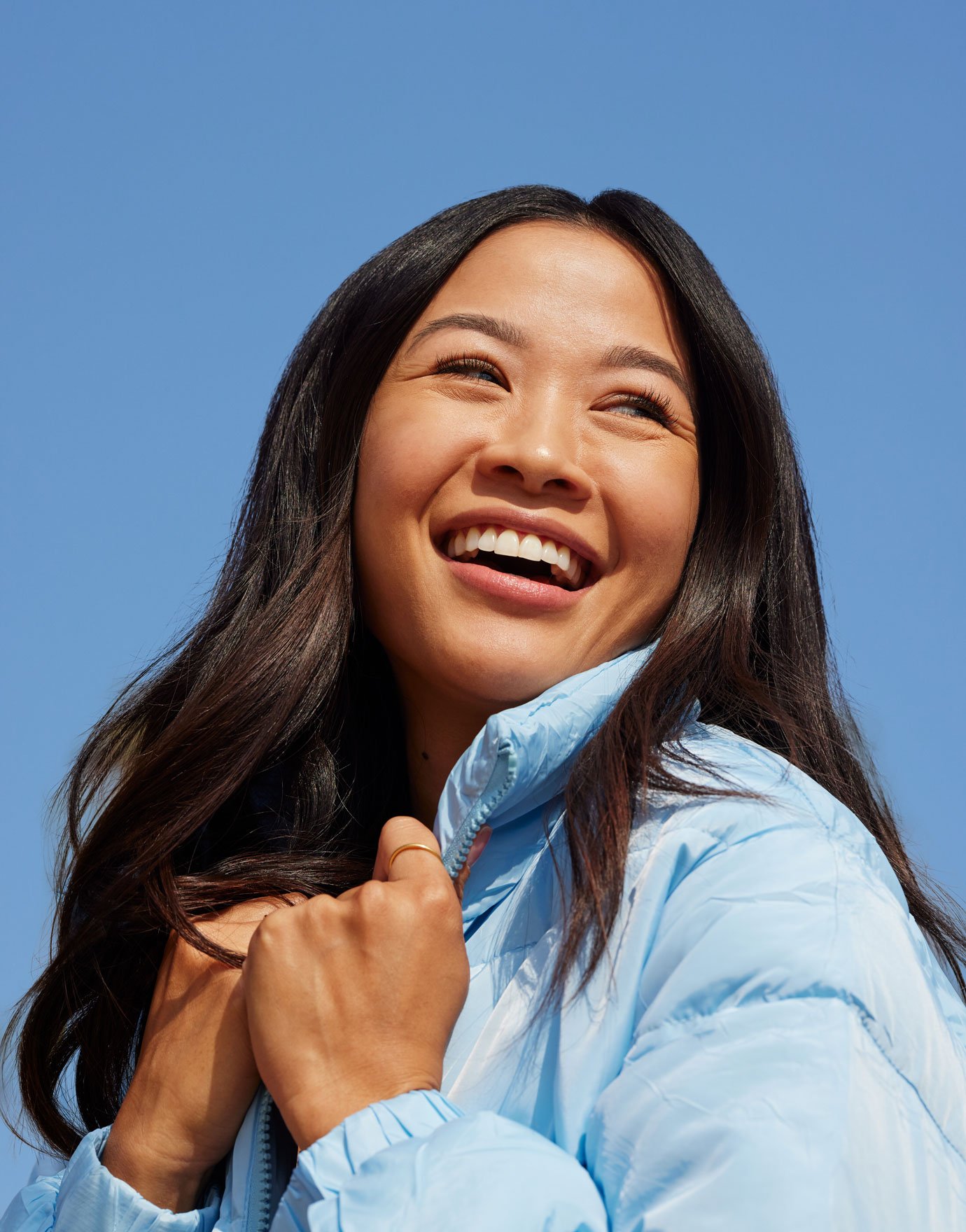 Woman in a light blue puffer jacket is smiling against a blue sky