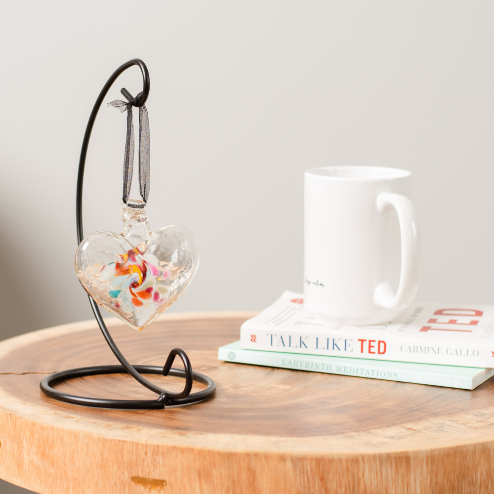 Heart of Memories on a Small Curved Single Ornament Holder. Displayed on a wooden side table beside a white mug on a stack of books. 