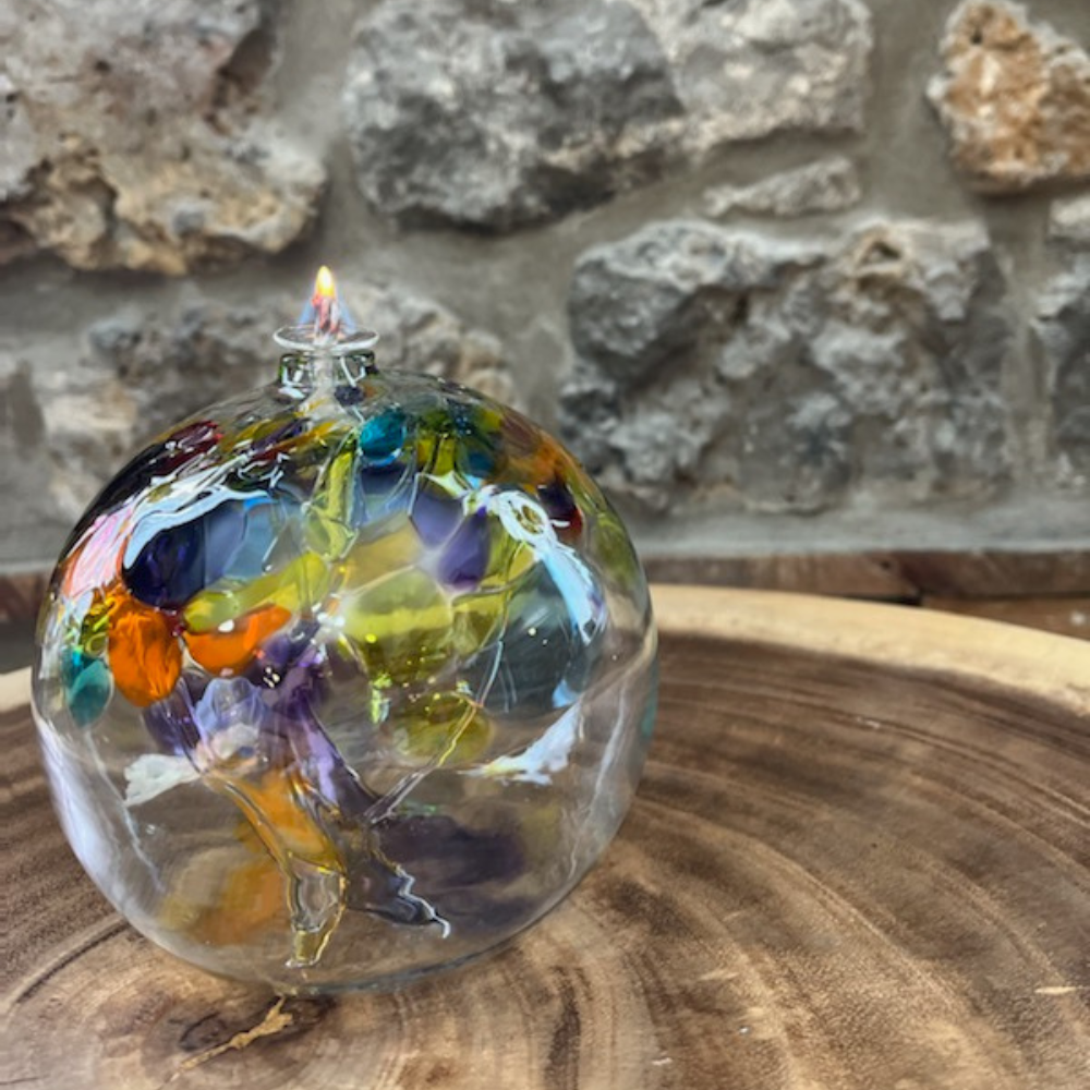 Clear glass flat bottom orb with blue and purple glass pulled through the middle and yellow, red, purple, orange, green and blue bits on top on a transparent background.