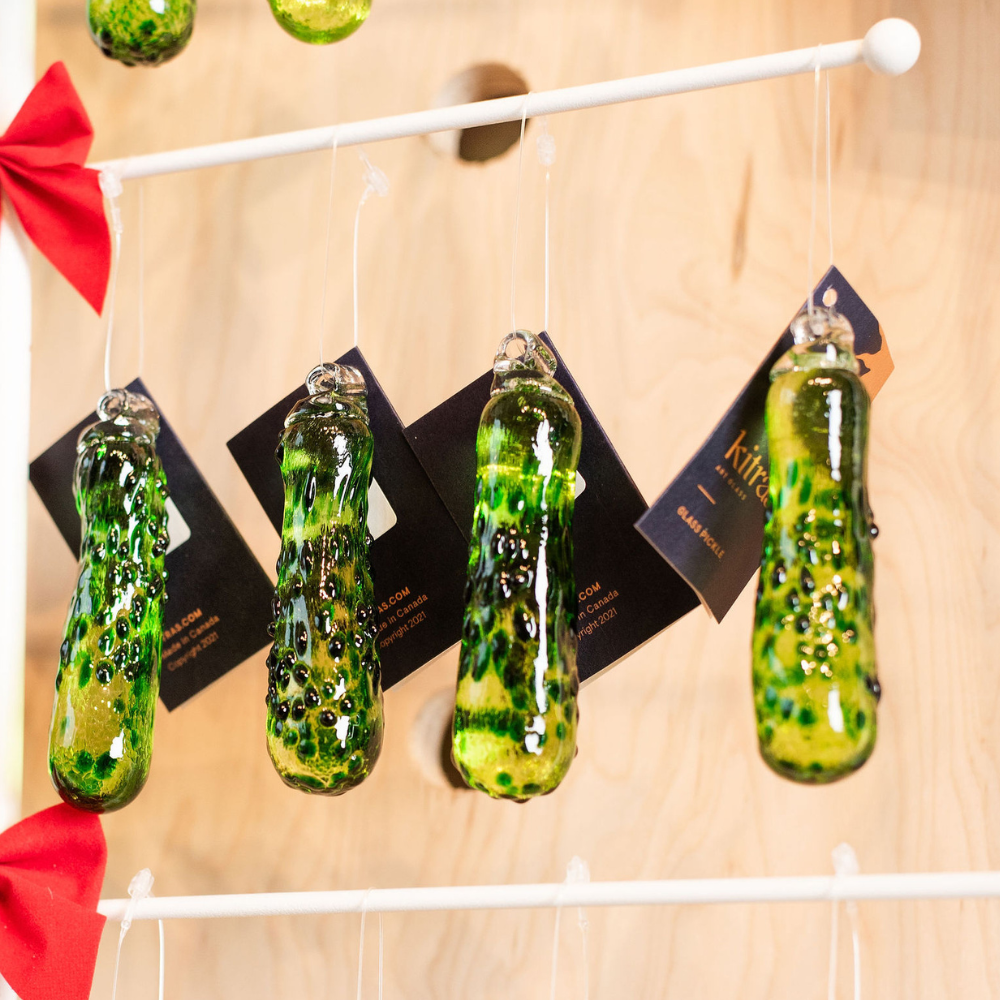 Four green Glass Pickles hanging from a white rod with a wood background.