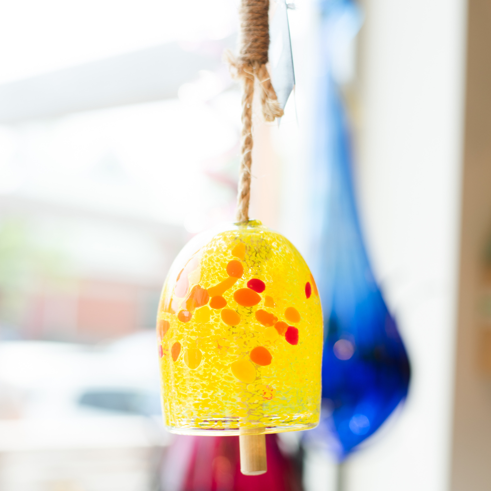 Opaque yellow bell with yellow, orange and red spots with a rope and wood toggle in front of a window.