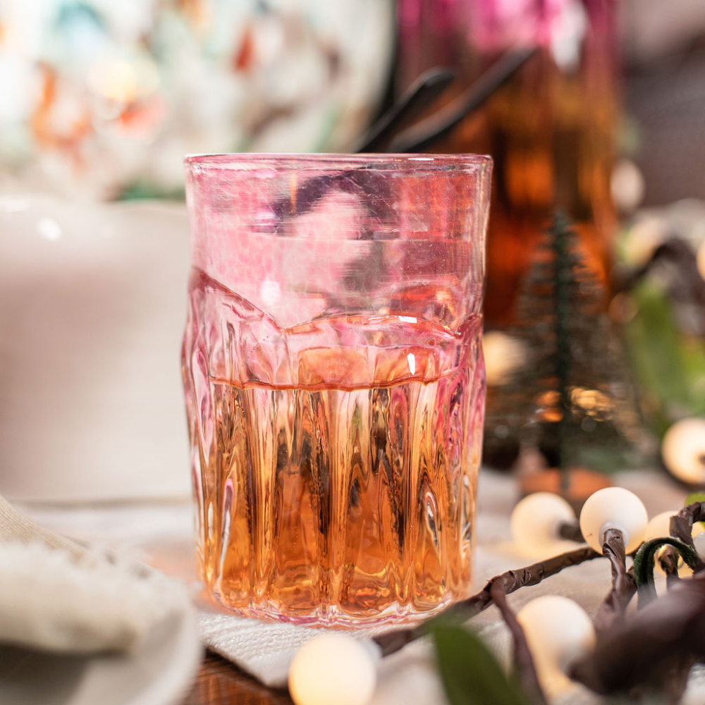 Glass with clear bottom and pink glass top, half filled with an amber liquid, on a holiday table setting.