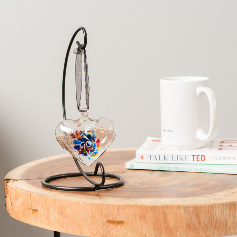 Heart of Wonder on a Small Curved Single Ornament Holder. Displayed on wood end table with a white cup resting on a stack of books. 