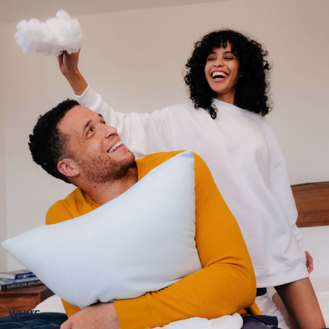 A man holding a Slumber Cloud UltraCool Pillow and laughing while a woman holds fiber filling over his head and laughing