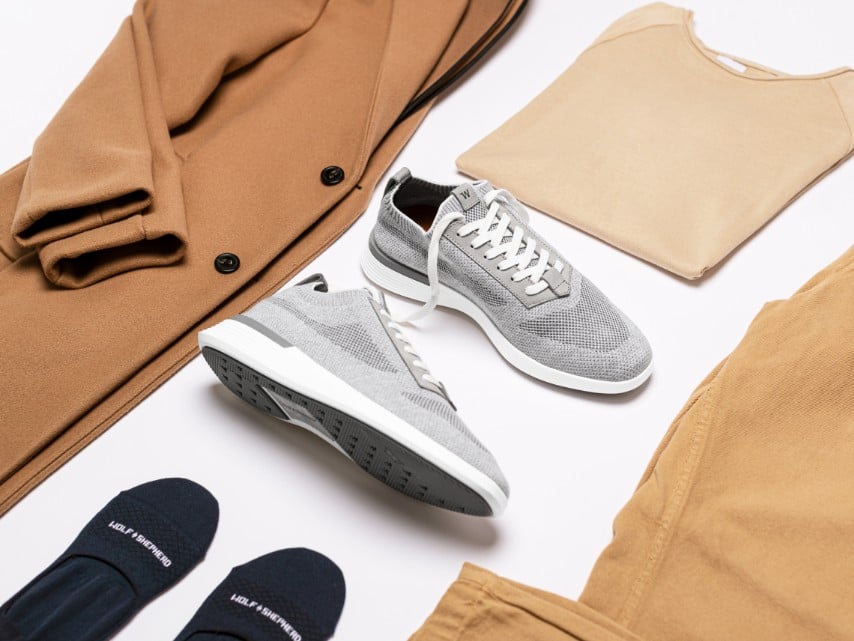 Flat lay image of supremeknit trainer in gray with socks, sweaters, and a coat