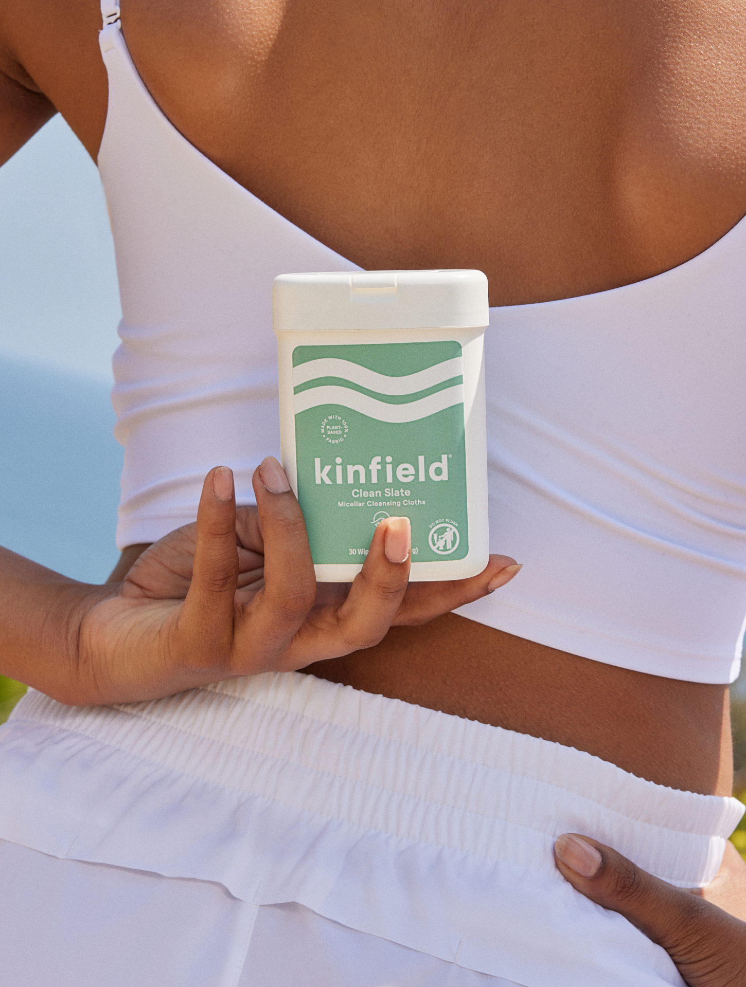 Woman holds Kinfield Cleansing Wipes behind her back with view of the ocean