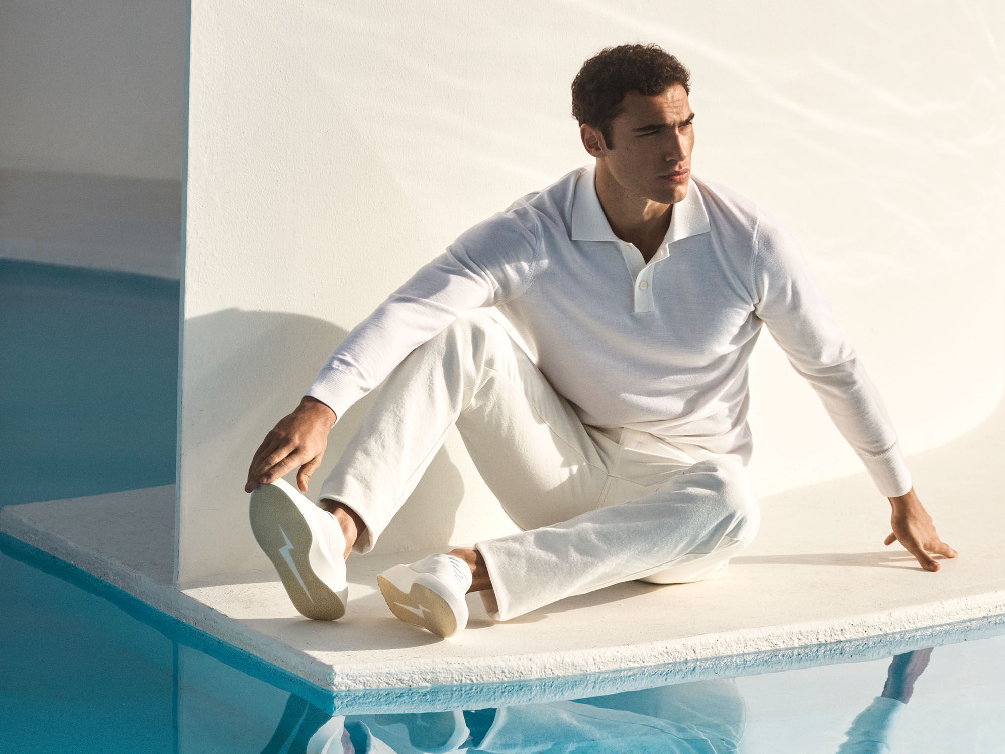 Man stretching sitting on a white floor wearing cruise lace up in white