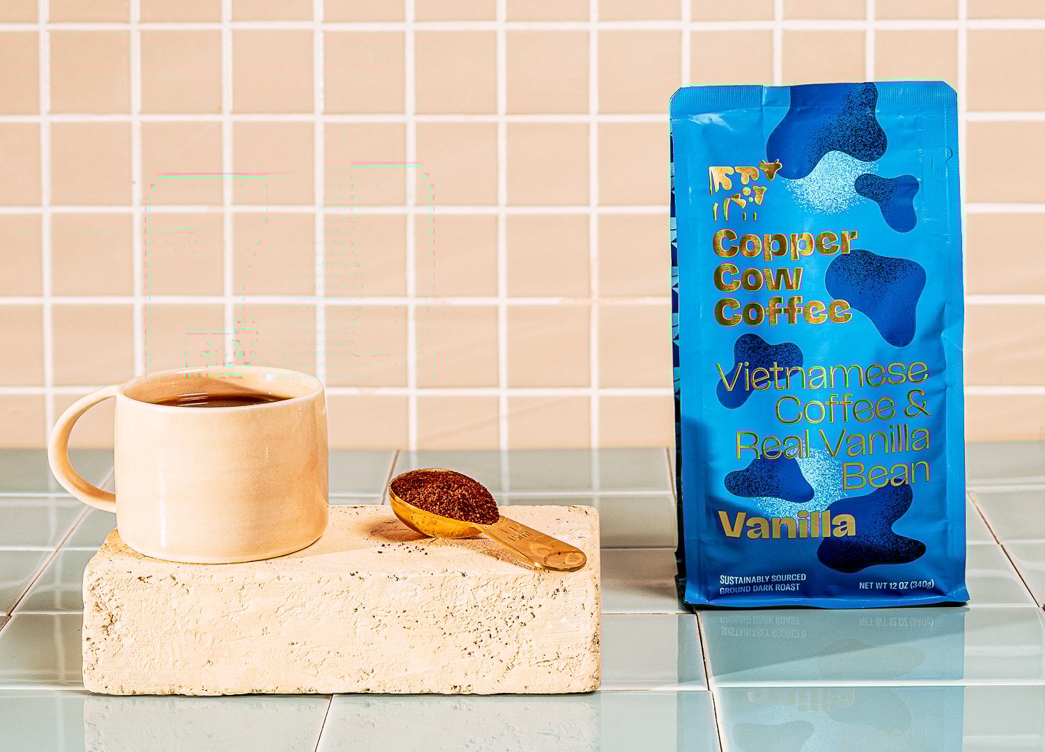 Copper Cow Coffee Vanilla ground bag with coffee grounds and warm cup of coffee in a ceramic mug