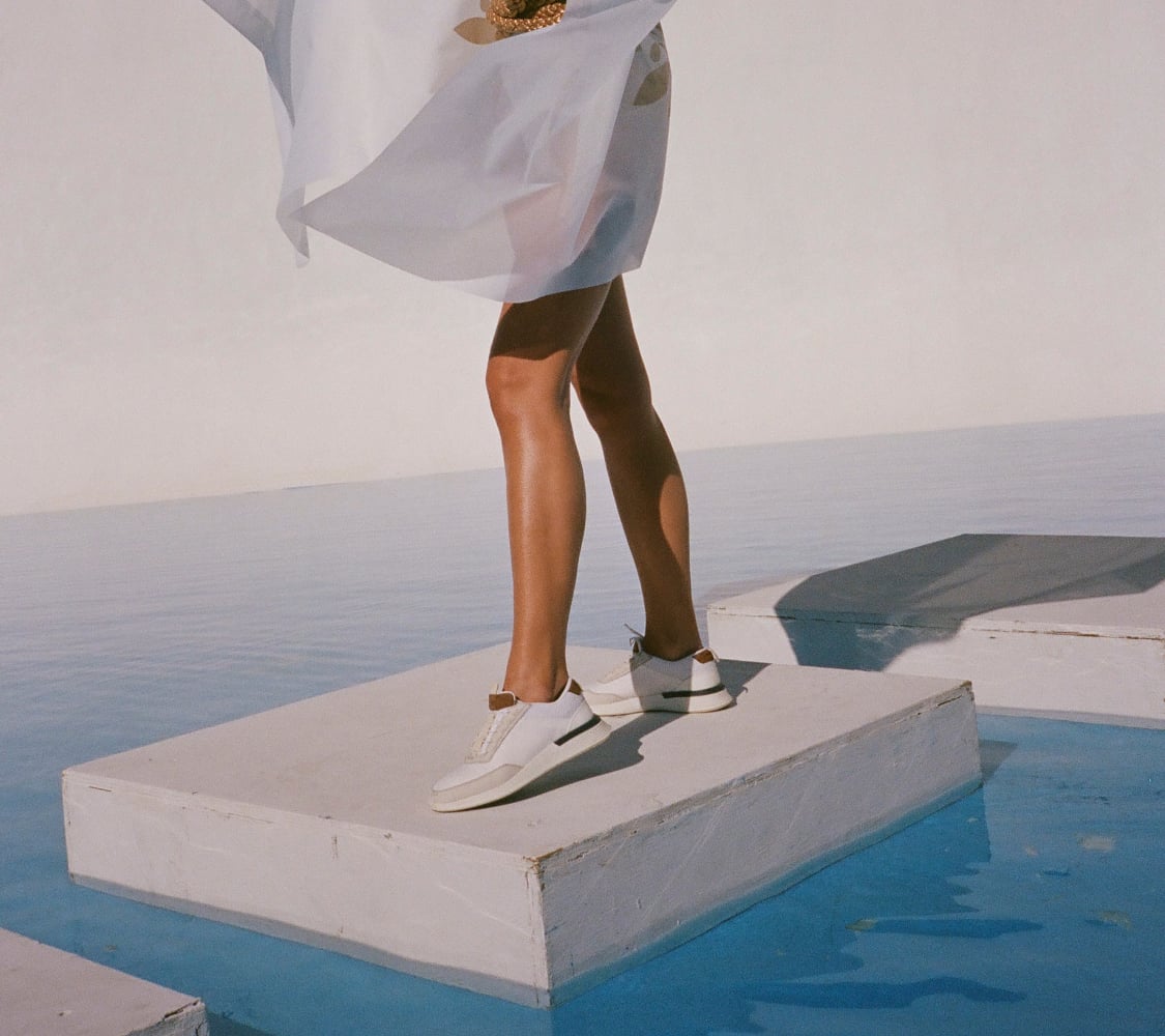 Knee down view of woman standing on white pedestal wearing Women's Hybrid Dress shoe Crossover Victory Trainer in White