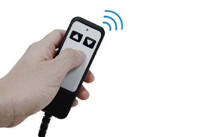 A hand holds a black and white remote control with two arrow buttons for the So Lite Portable Lift from Journey Health & Lifestyle. Blue lines above the remote indicate a wireless signal, likely powered by a lithium-ion battery, set against a plain white background.
