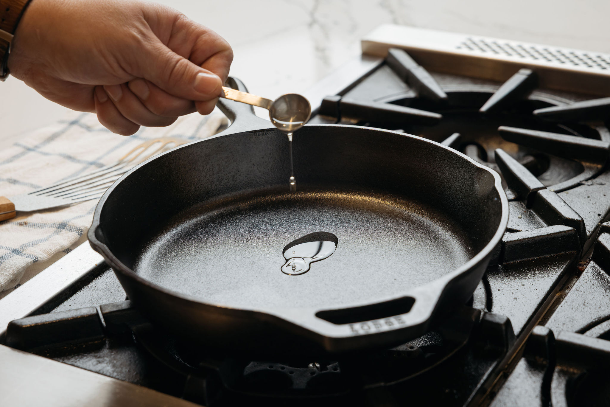 A person sets the bottle of Seasoning Spray onto the countertop in front of a Lodge Cast Iron Skillet.