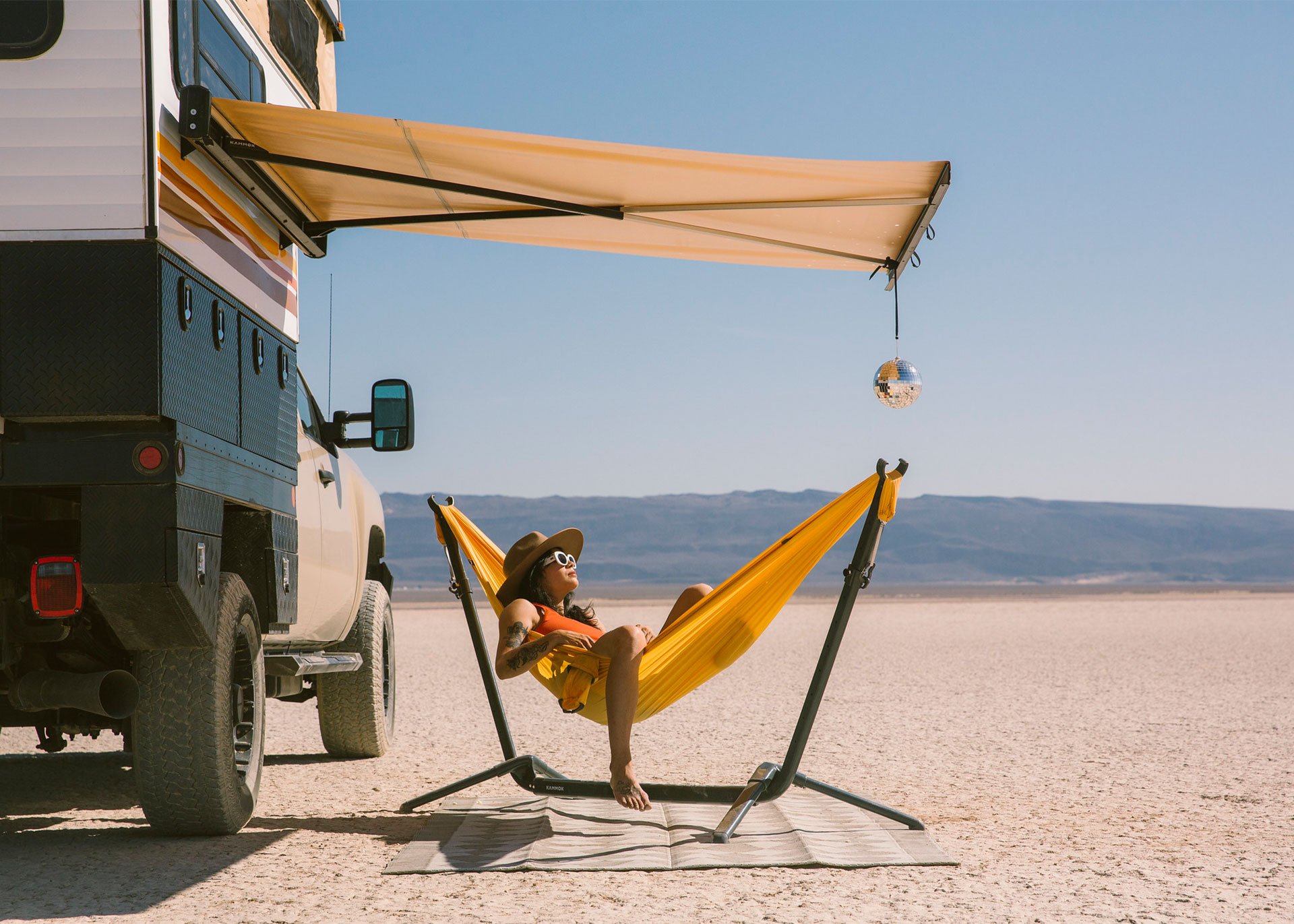 Woman sitting in Swiftlet portable hammock stand under seven foot Crosswing awning.