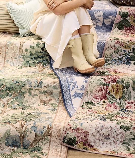 Lots of runners from the Highgrove by Sanderson x Hug Rug collaboration draped along steps, with someone sat on them wearing a dress and wellies. 