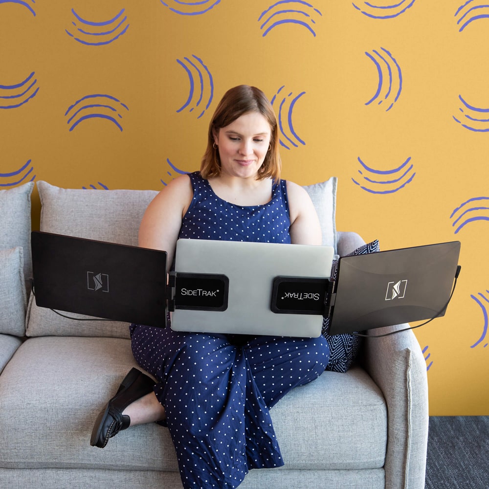 a woman working on a couch with a sidetrak swivel multi monitor set up with hub
