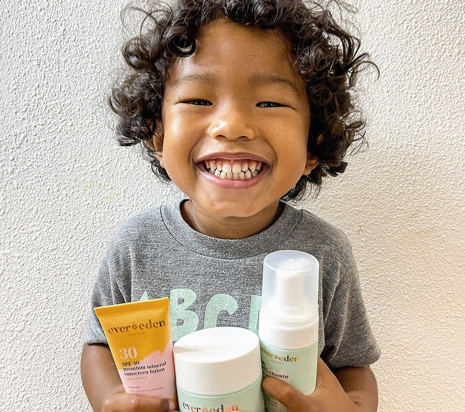 Smiling child holding Evereden skincare products.