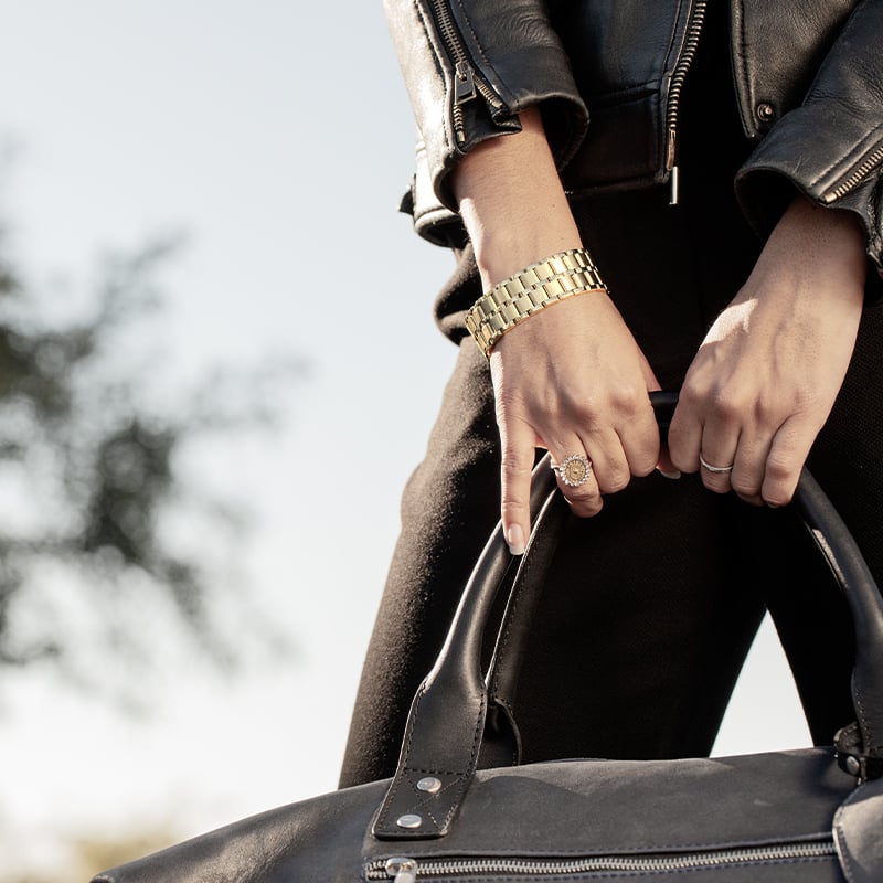 Woman wearing black leather jacket holds black leather bag with The Confidante watch in All Gold on wrist