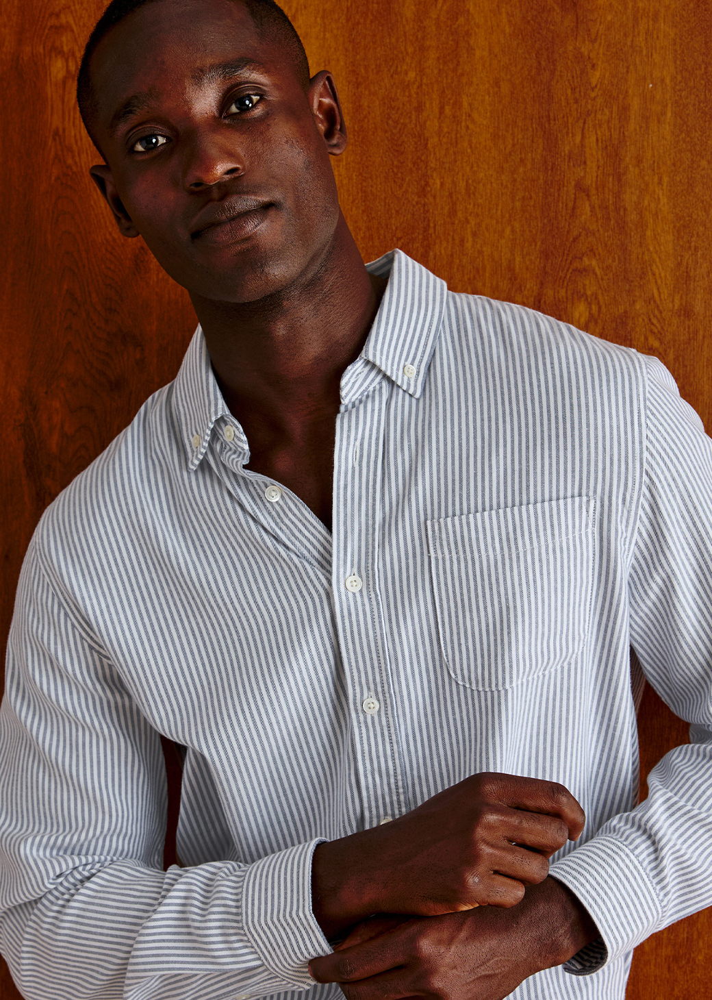 Man wearing a blue and white stripe button down shirt against a brown background.