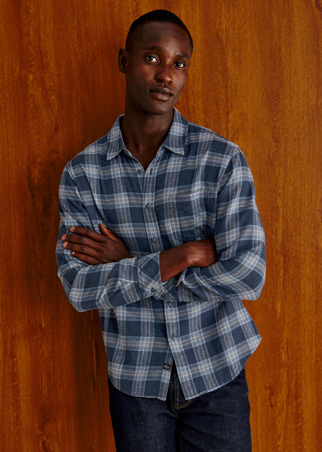 Man wearing a plaid blue long sleeve shirt against a brown background.