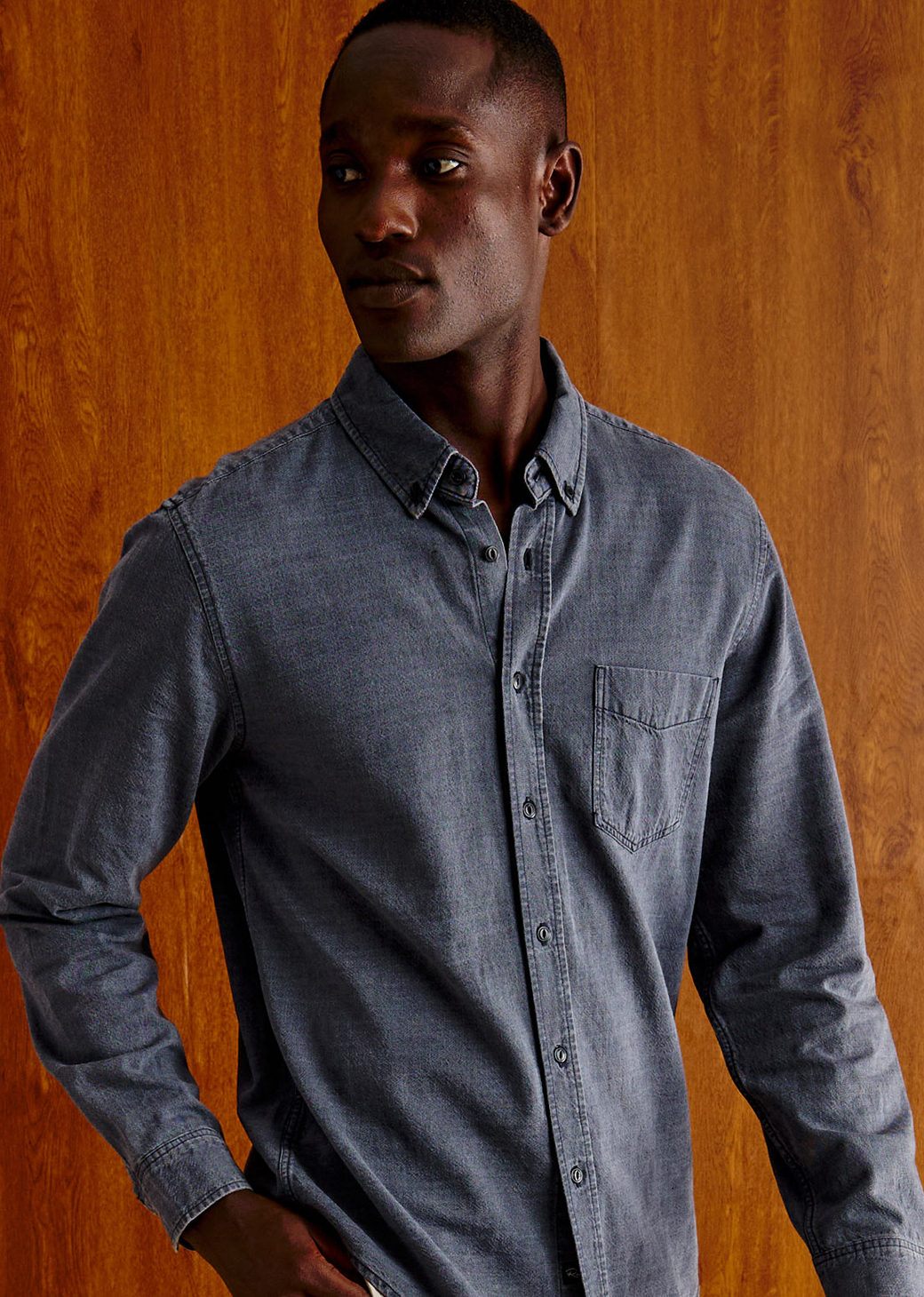 Man wearing a blue long sleeve shirt against a brown background.