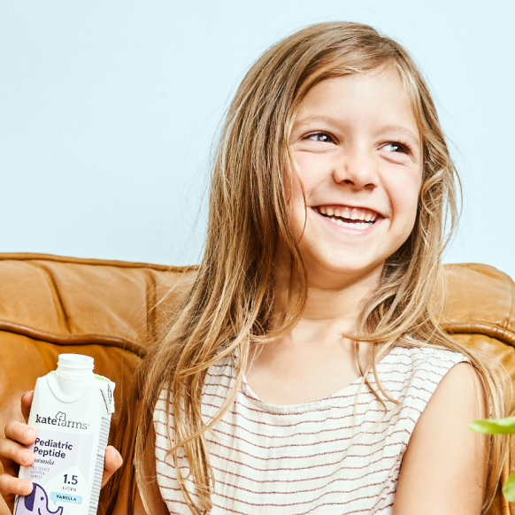 Young child smiling holding a carton of Kate Farms Pediatric Peptide 1.5 formula