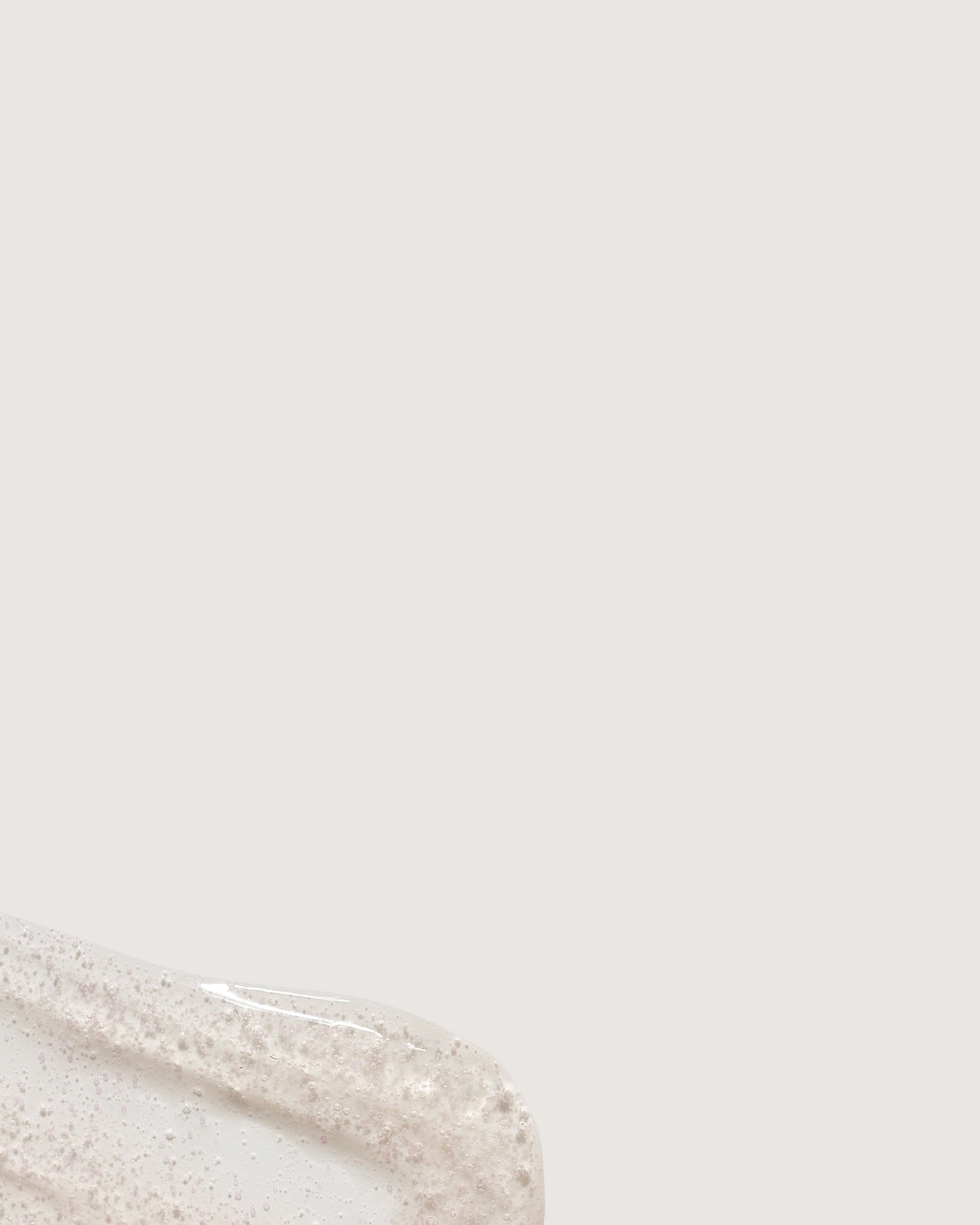 Background image of a formula swatch showcase the Rose Inc Skin Clarity Exfoliating Cleanser's Jojoba bead texture.