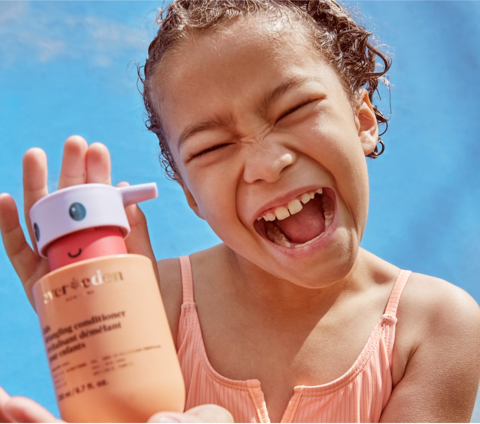 Smiling child holding a kids hair care bottle.