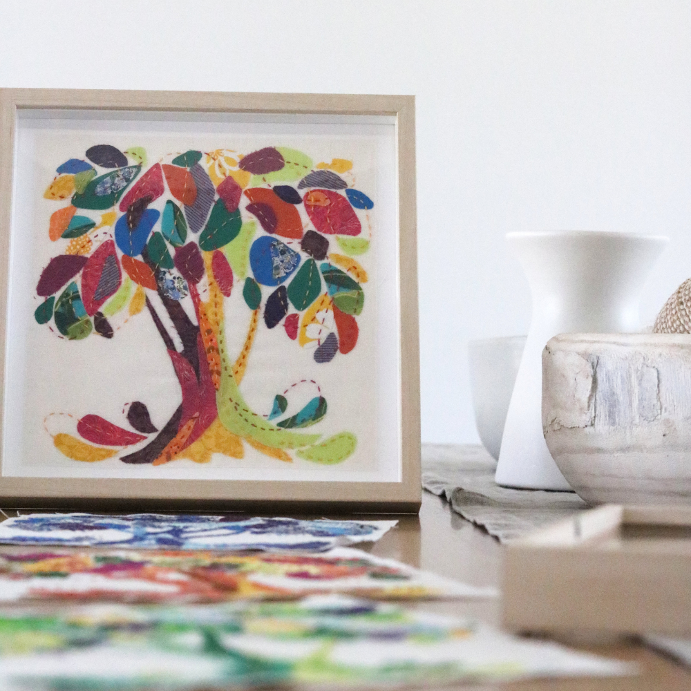 yellow, blue, green, purple, orange and lime fabric tree sewn on a white background, with a brown frame n on a table