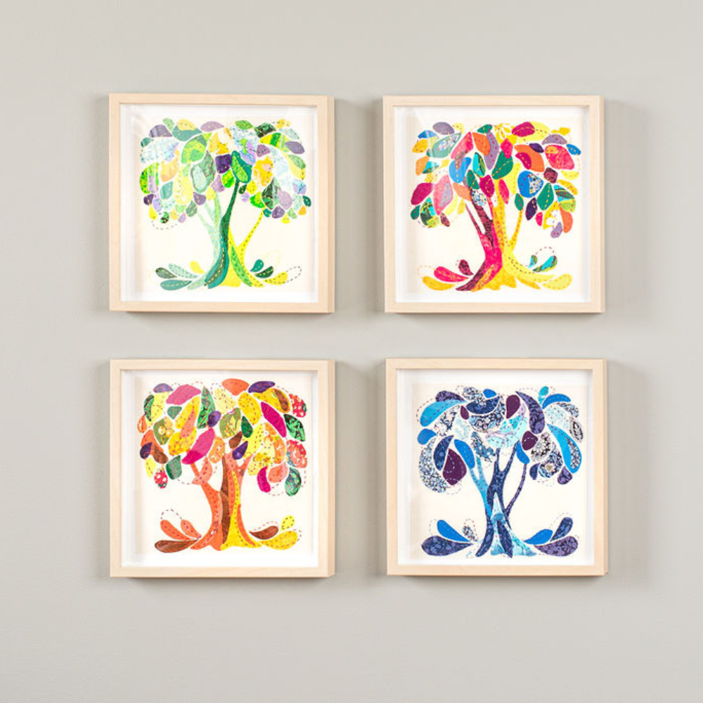 Four fabric trees sewn on a white background, with a brown frame.