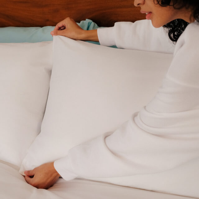 A woman making her bed and putting Slumber Cloud Core Pillow Covers on her pillows