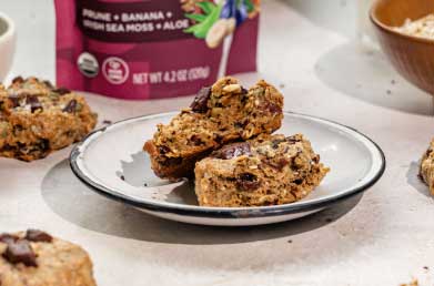 A plate of homemade breakfast cookies with visible chunks of chocolate, next to a package of Navitas Organics Superfood+ Digestive Blend.