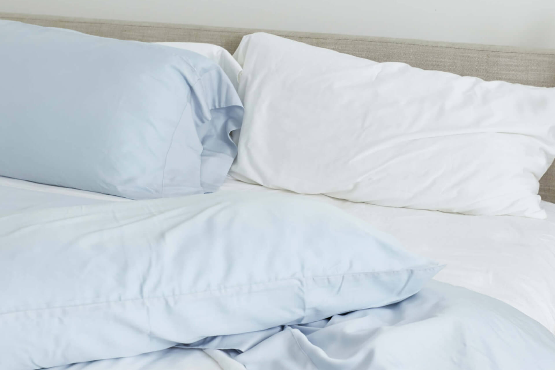 A messy bed with Slumber Cloud Performance Pillowcases in white and light blue