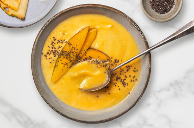 A yellow smoothie bowl topped with mango slices and seeds.