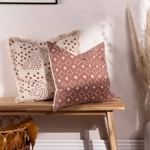 Brown cushions with woven spotted and abstract designs, propped on a wooden bench in front of a white background.