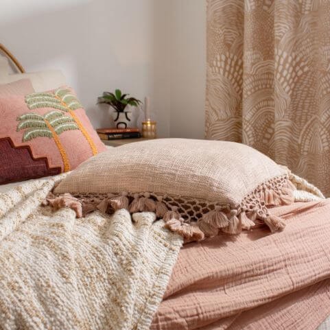Neutral home decor including a tasseled boho cushion in a blush pink shade, displayed on a boho style bed.