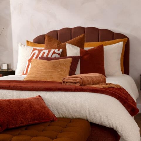 Neutral home decor layered in a luxe style bedroom, including a bouclé duvet set, brown and red scatter cushions, and a rust red faux fur throw.