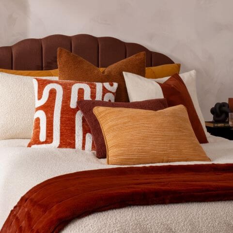 Luxe style scatter cushions displayed on a bouclé duvet cover set, along with a faux fur throw and other neutral home decor.