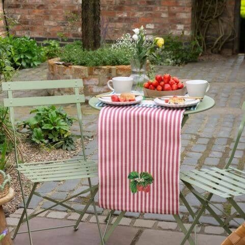 A small garden patio space decorated with a bistro sit and outdoor table linen with a striped strawberry design.