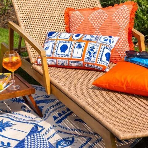 A small garden patio space decorated with a woven sun lounger and bright tropical outdoor cushions.