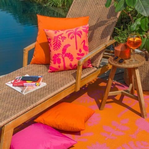 A small garden patio space decorated with a woven sun lounger and bright orange tropical outdoor cushions.