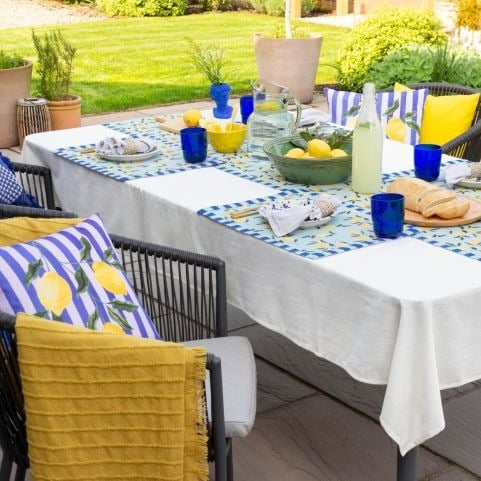 A small garden patio dining area decorated with a white table cloth, and outdoor cushions and table linen with a vibrant lemon design.