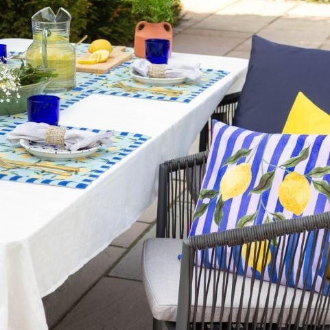 A small garden patio dining area decorated with outdoor cushions and table linen with bright fruit designs.