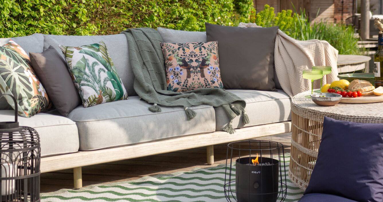 An outdoor entertaining area decorated with a garden sofa, outdoor cushions and an abstract outdoor rug.