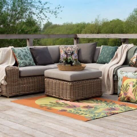 An outdoor entertaining area in a living room style, featuring a garden sofa, outdoor cushions, throws and an outdoor rug.