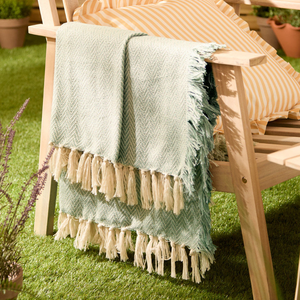 Soft woven herringbone design with a tasselled trim for effortless style in green on a wooden outdoor chair
