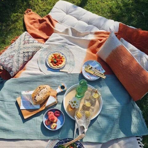 An outdoor entertaining area in a garden picnic style, featuring a muslin throw blanket and dip-dye style cushions.