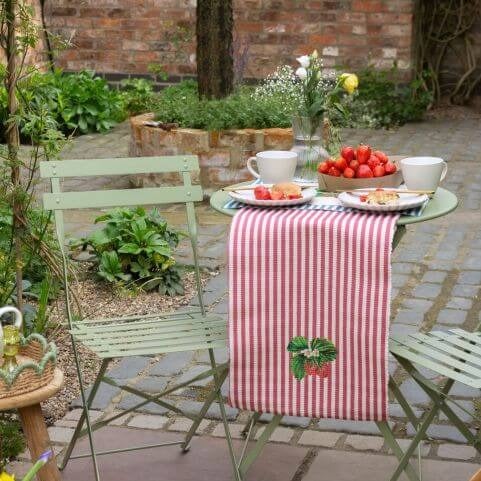 An outdoor entertaining area styled for a garden picnic, featuring a small bistro set decorated with striped outdoor table linen.