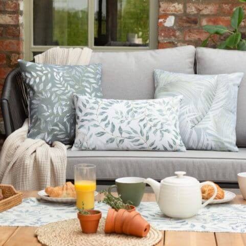 A coffee morning scene prepared in an outdoor entertaining area, featuring neutral floral outdoor cushions and a throw blanket.