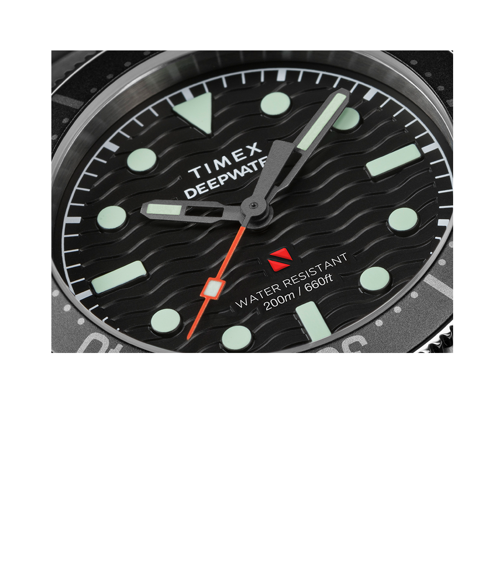 Extreme close-up of the black dial on the Timex Deepwater Reef 200. Highlights include bold luminescent hour markers, the red diver-down flag, and wave-textured detailing, with crisp printing of “WATER RESISTANT 200m / 660ft.”