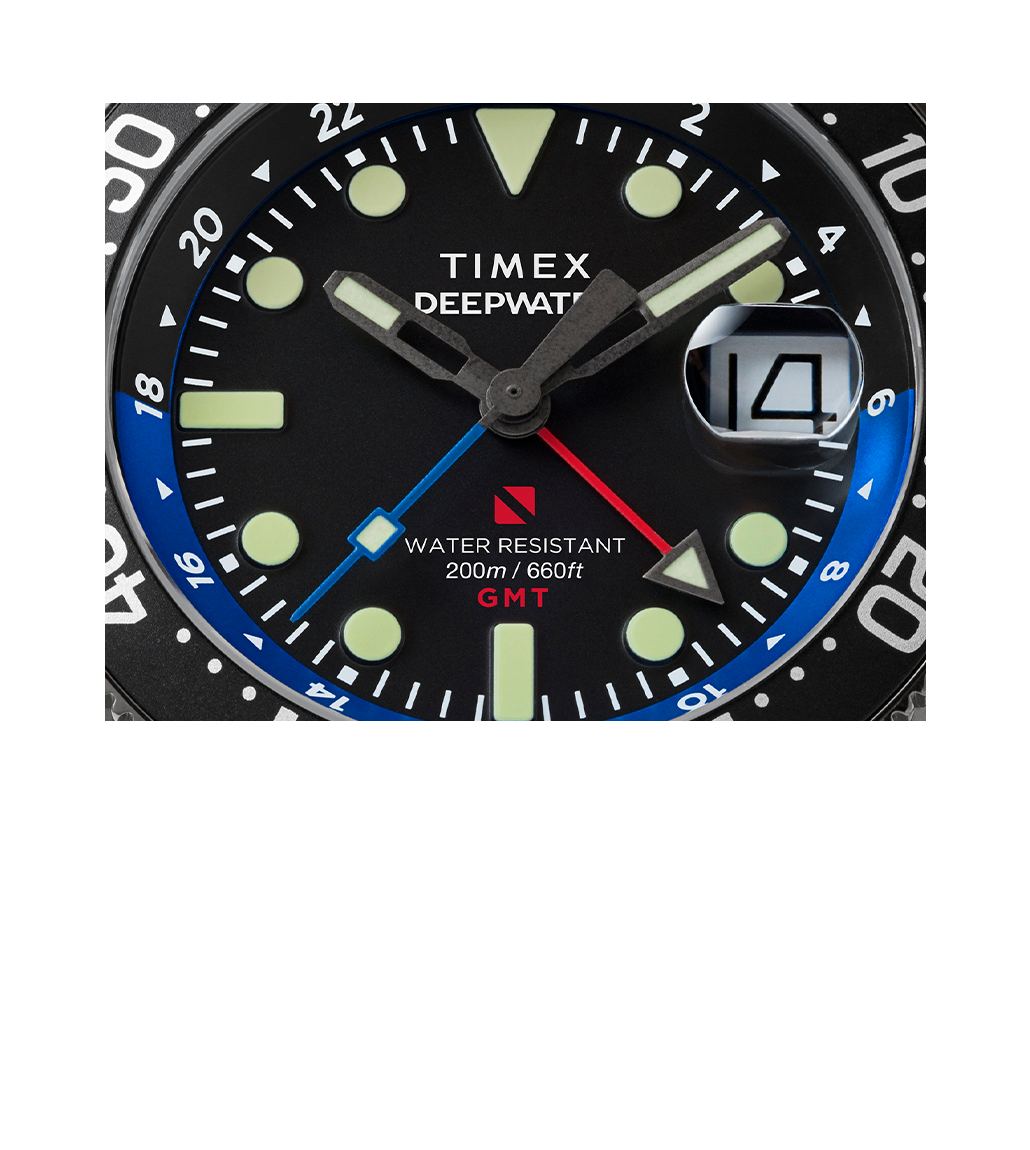 Close-up of the Deepwater Reef GMT dial. Shows bold luminous indices, red GMT hand crossing a blue fourth hand, printed text “WATER RESISTANT 200m / 660ft GMT,” and cyclops date lens.